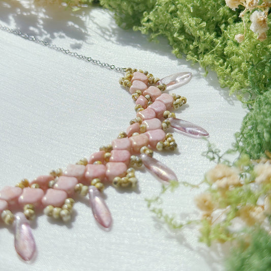 Close-up of a pink beaded statement necklace with floral petal pattern and translucent glass drop details, showing texture and craftsmanship