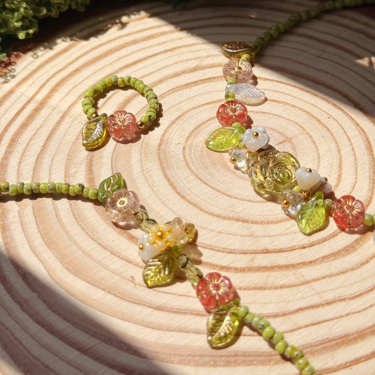 Jewelry set with green and floral beads on a wooden surface with moss