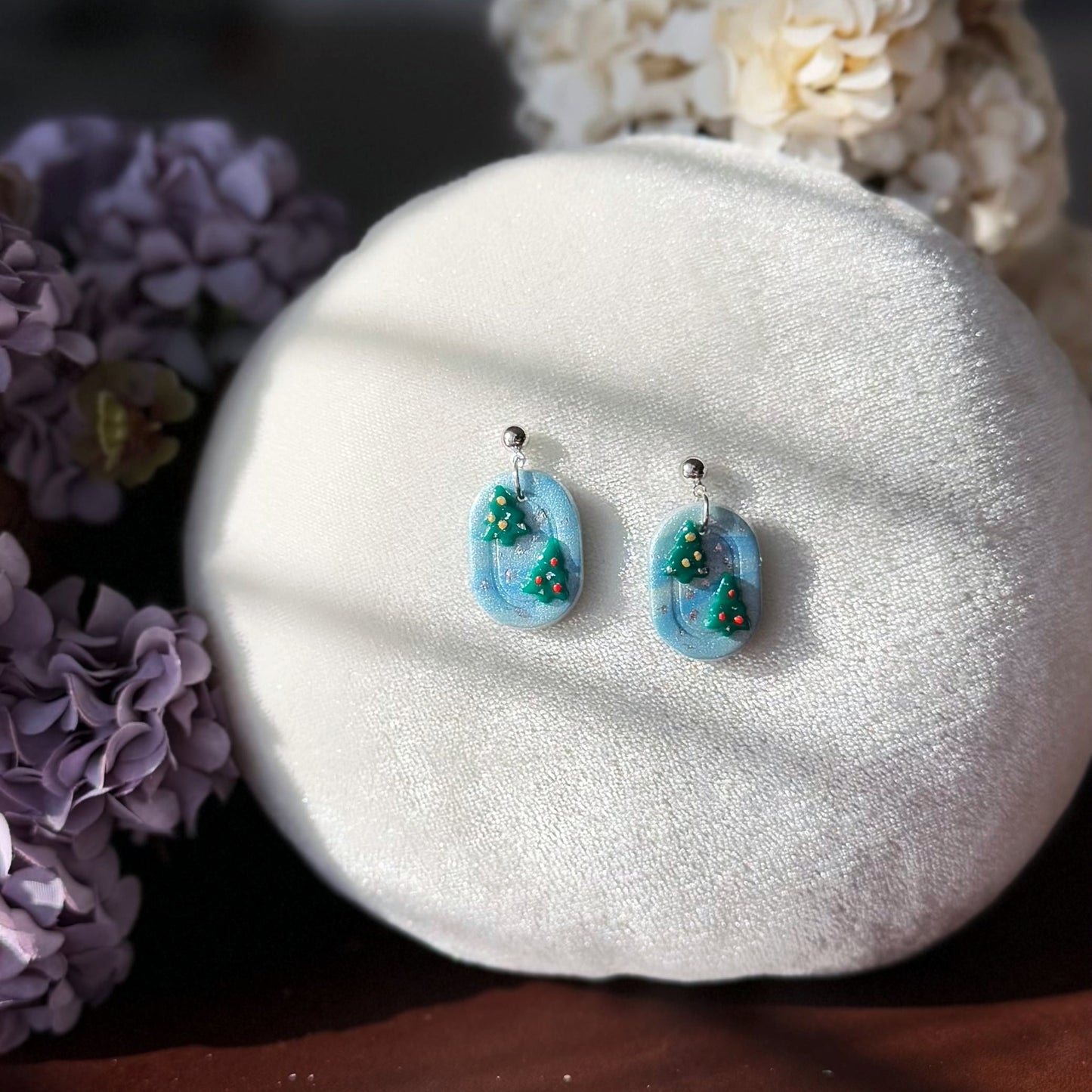 Pair of earrings with two Christmas trees design on a white stone with flowers in the background