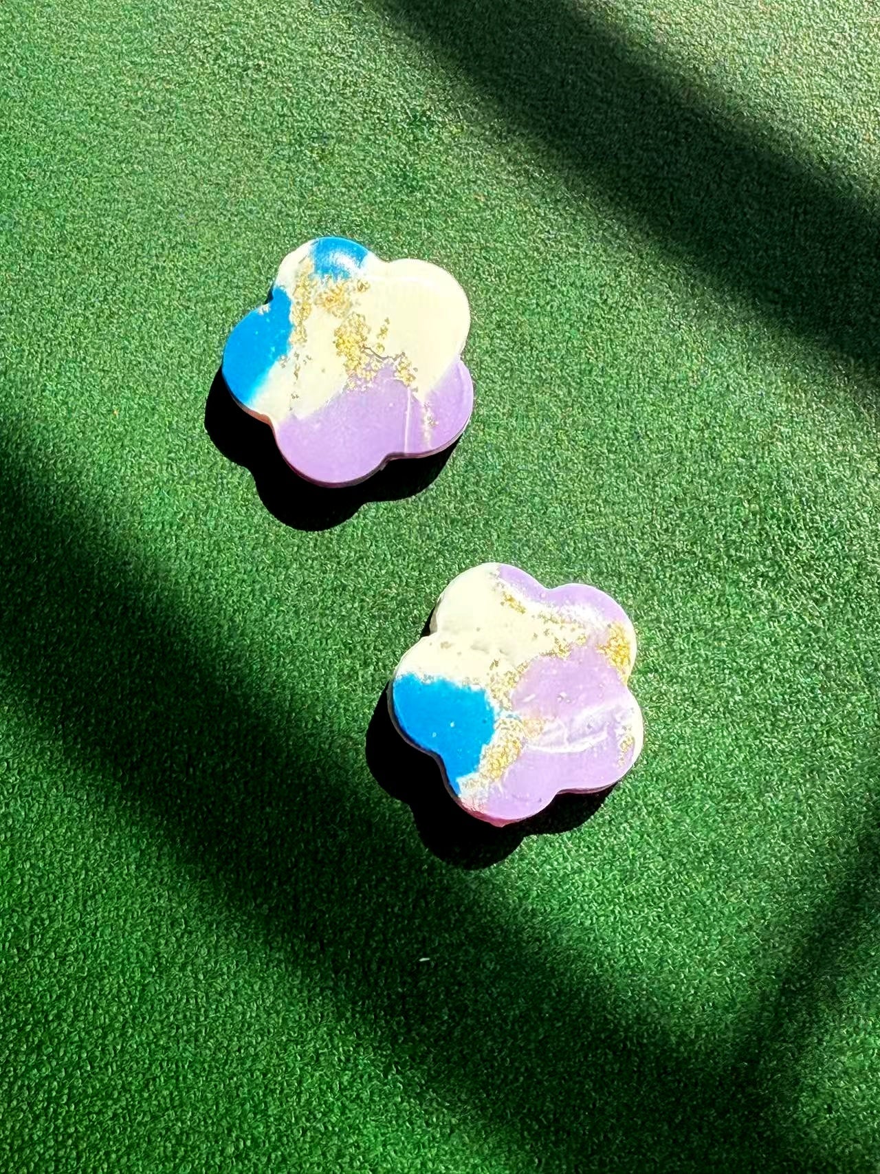 A pair of flower-shaped earrings with a colorful marble effect on a green surface