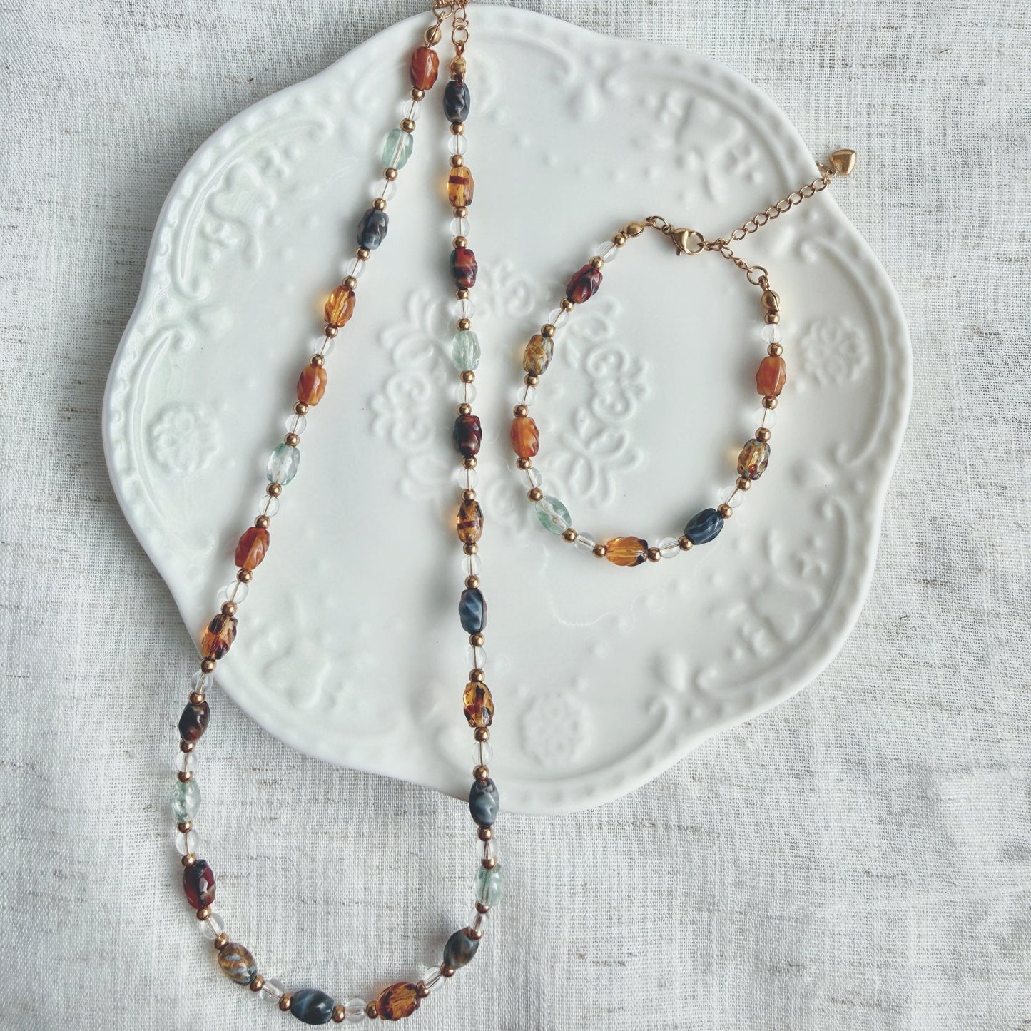 Beaded necklace and bracelet set on a textured white plate with a light gray background