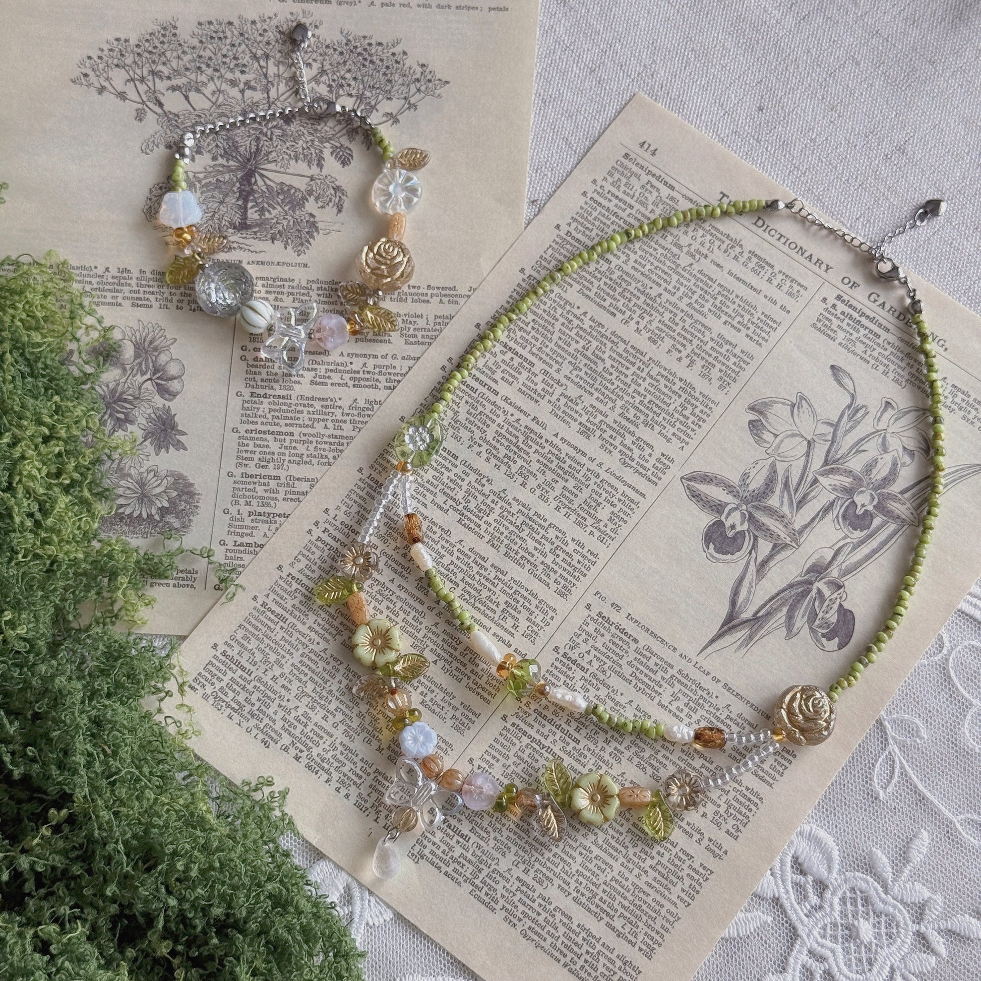 A beaded necklace and matching bracelet displayed on vintage book pages with a green plant sprig. The jewelry features light green beads, clear Czech glass beads, amber-colored beads, and a small gold rose charm.