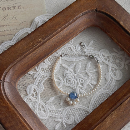 A delicate freshwater pearl bracelet with a natural Kyanite centerpiece, displayed inside a vintage wooden frame over white lace fabric.