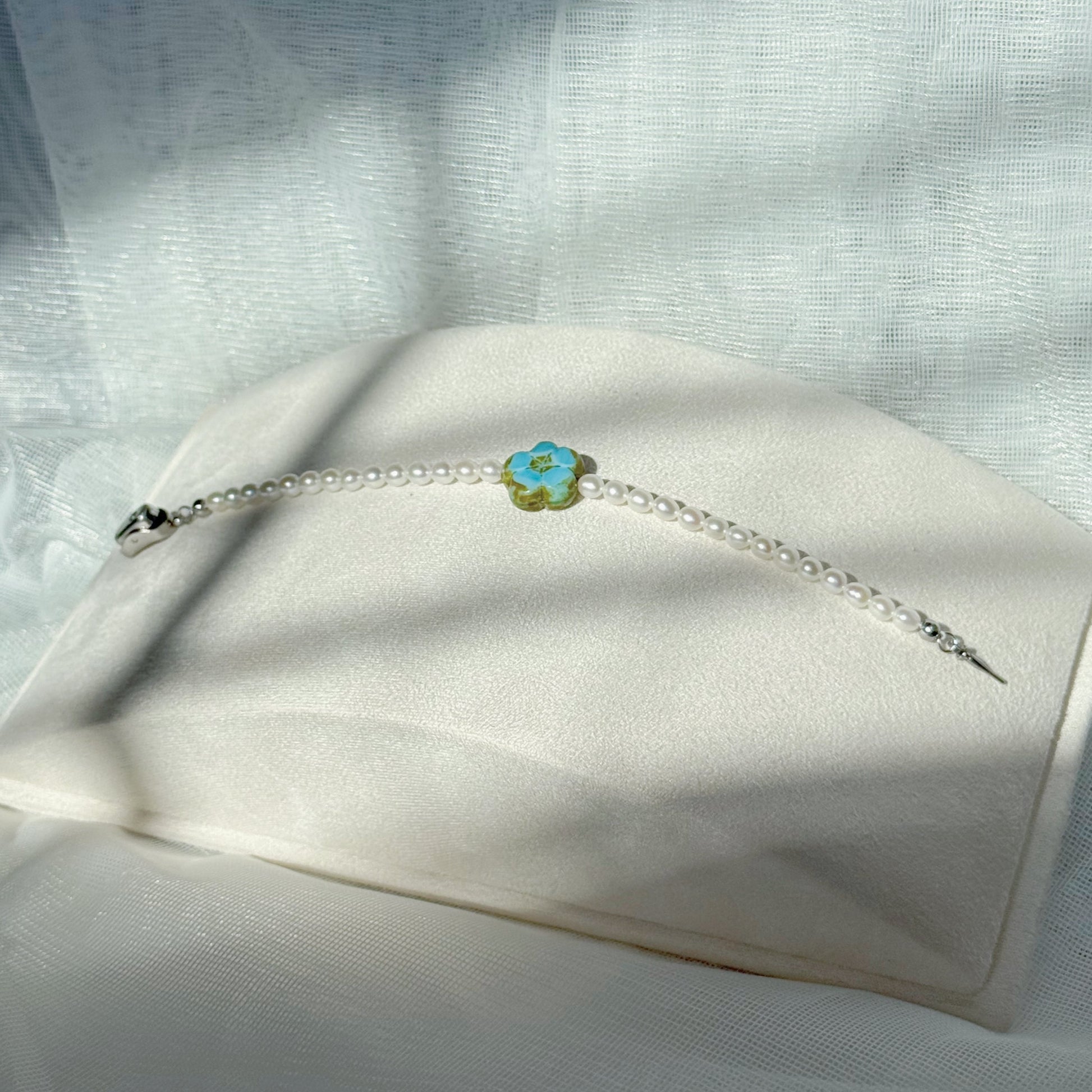 Pearl beaded bracelet with a blue Czech glass floral centerpiece, minimalist handmade jewelry on a soft fabric background