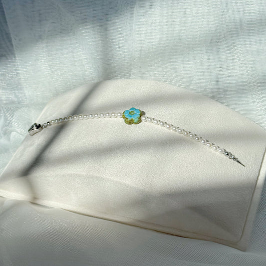 Pearl beaded bracelet with a blue Czech glass floral centerpiece, minimalist handmade jewelry on a soft fabric background