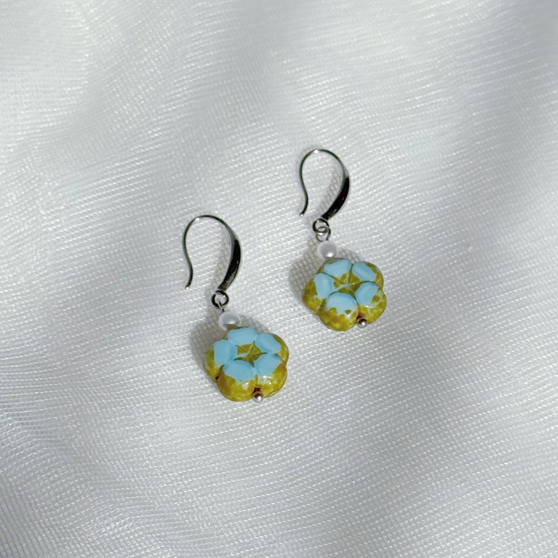 Pearl drop earrings with blue Czech glass floral charms, minimalist lightweight handmade jewelry on a soft fabric background