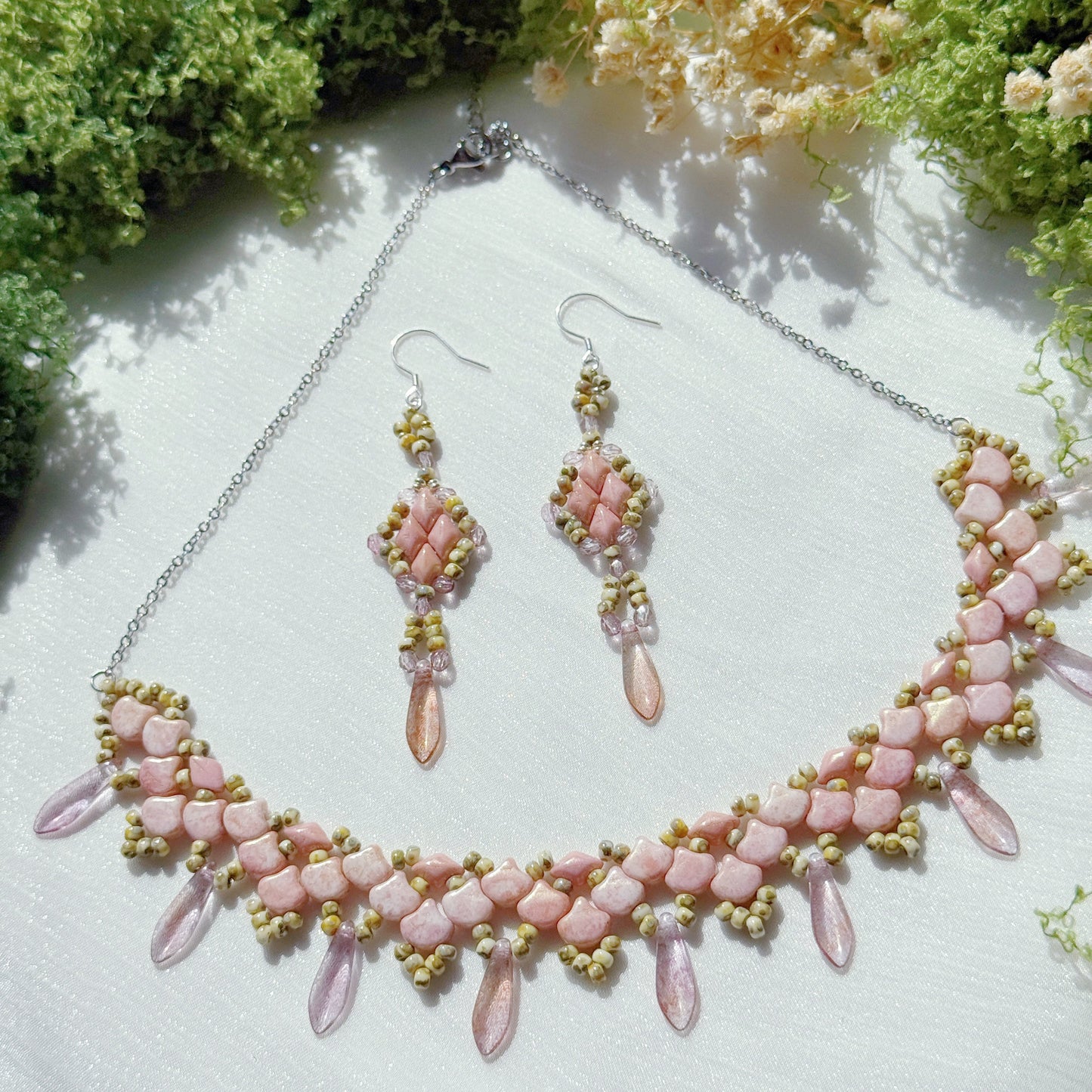 Pink beaded statement necklace with matching dangle earrings, featuring floral petal design and soft romantic tones, handmade jewelry on a textured fabric background