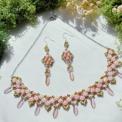 Pink beaded statement necklace with matching dangle earrings, featuring floral petal design and soft romantic tones, handmade jewelry on a textured fabric background