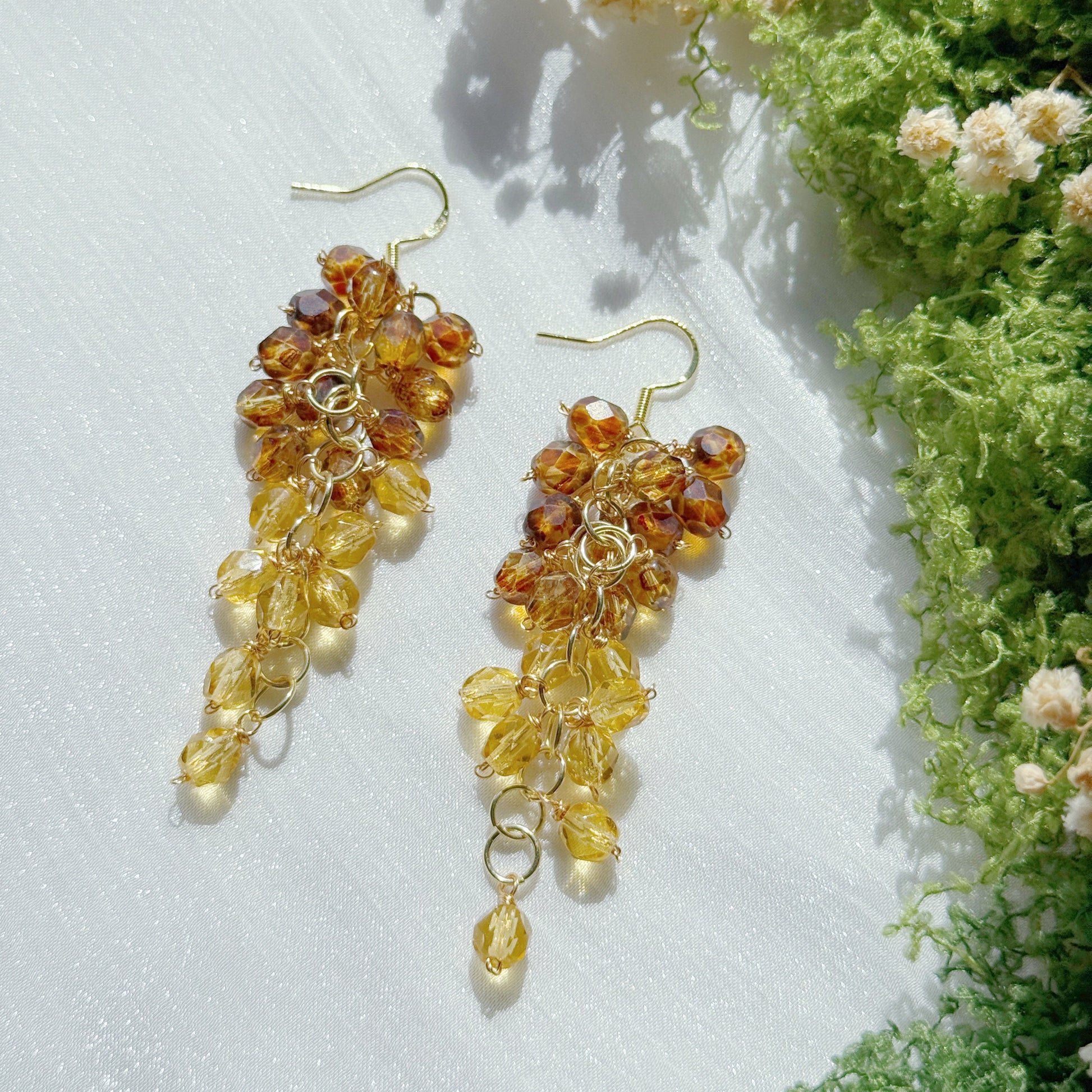 Gold and amber bead earrings on a white surface with greenery in the background