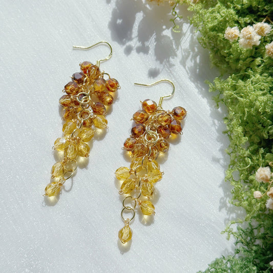 Gold and amber bead earrings on a white surface with greenery in the background