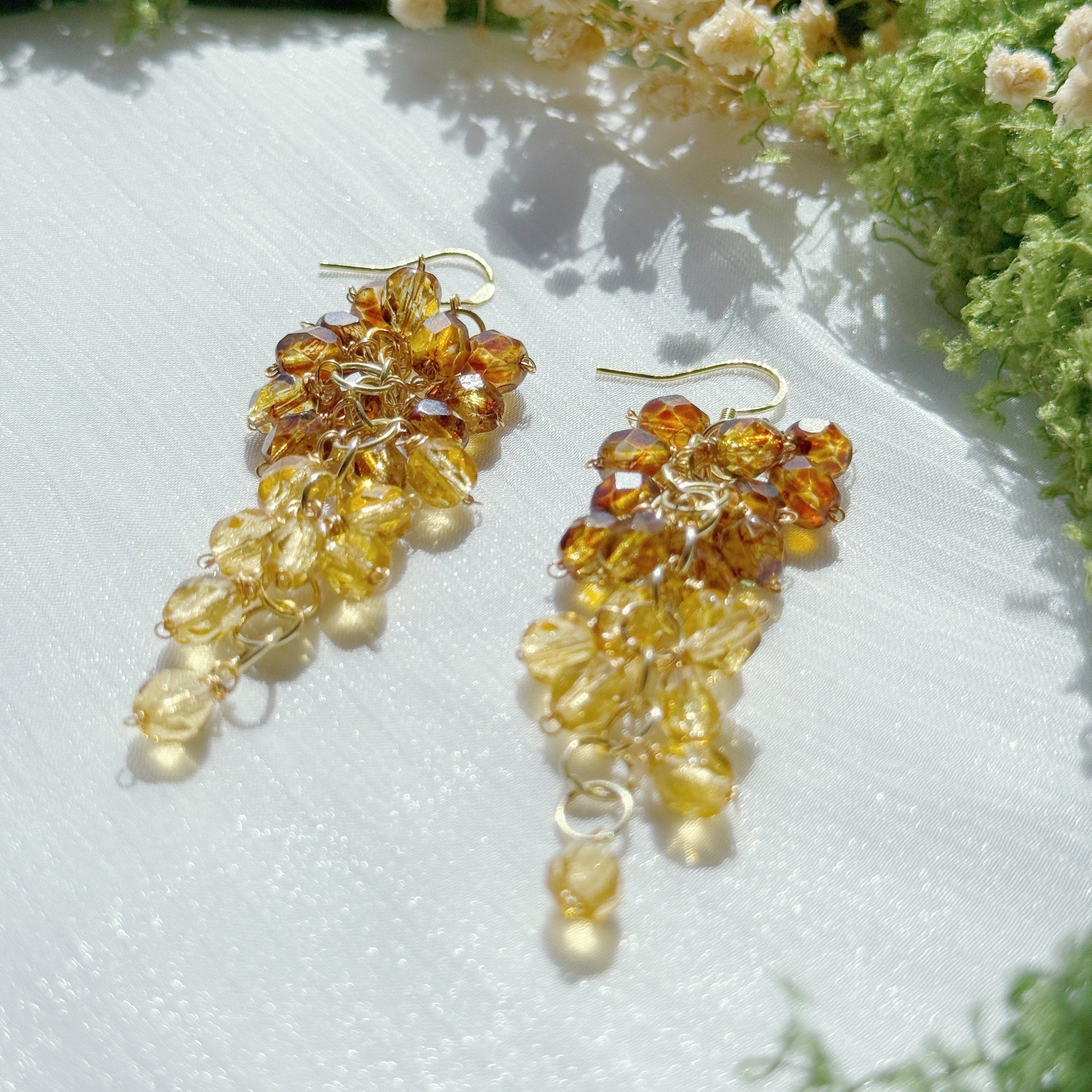 Gold and amber beaded earrings on a white surface with greenery