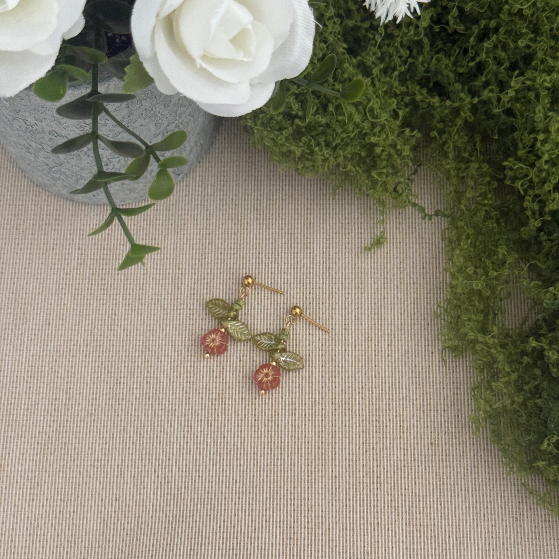 Beaded flower earring on a textured surface with flowers and greenery in the background
