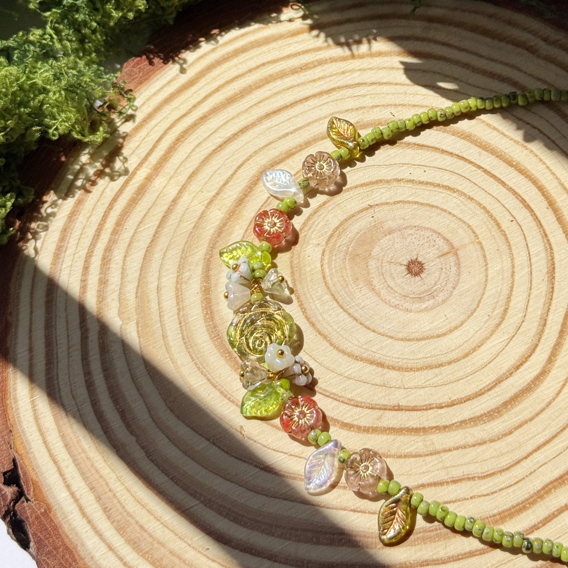 Choker with green and floral beads on a wooden surface with moss