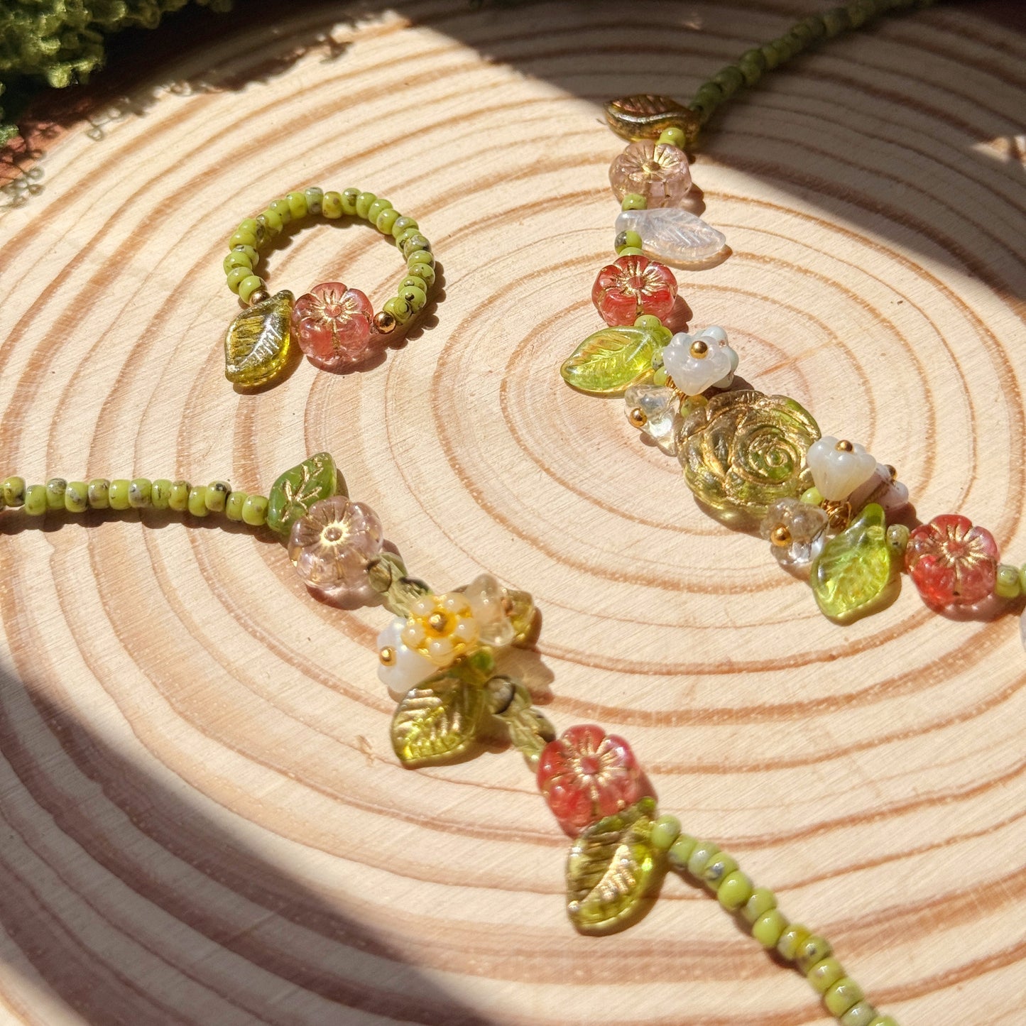 Beaded bracelet,ring, and necklace with green leaf beads and multicolor flower beads on a wooden surface