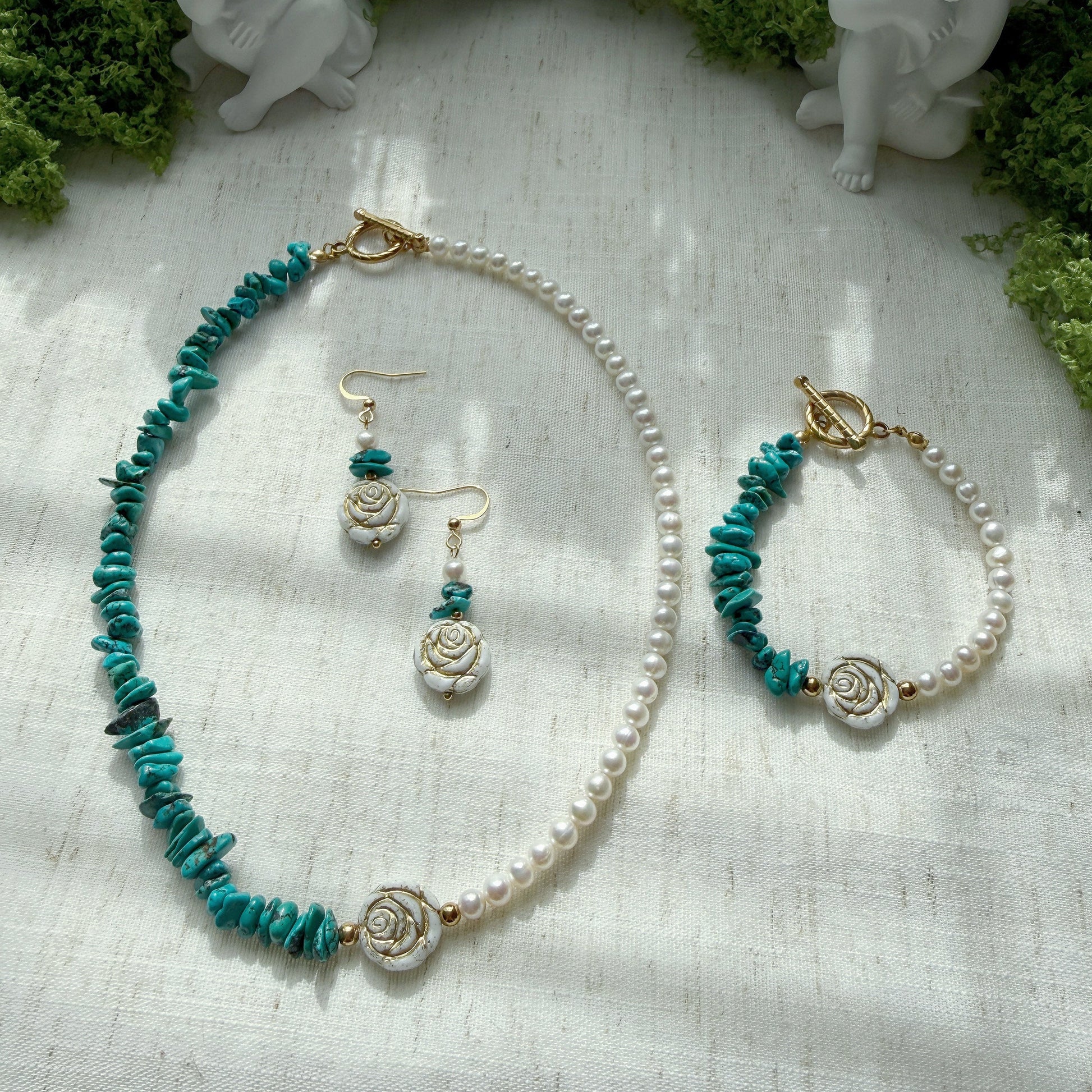 Handmade jewelry set featuring natural turquoise, freshwater pearls, and Czech glass rose beads, including a necklace, bracelet, and matching earrings displayed on a soft linen background.