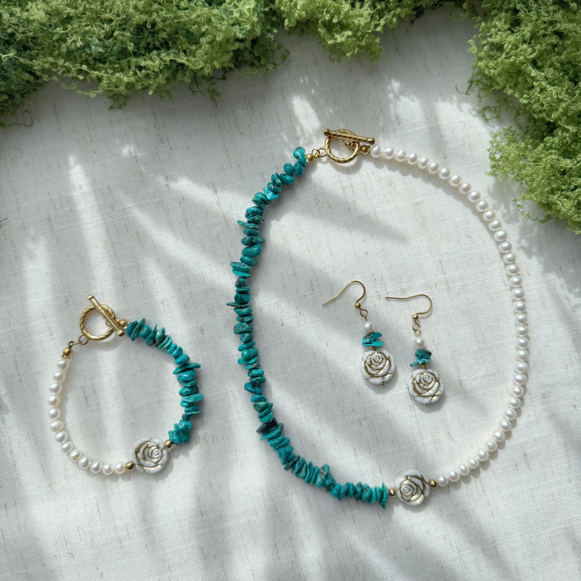 Handmade jewelry set featuring natural turquoise, freshwater pearls, and Czech glass rose beads, including a necklace, bracelet, and matching earrings displayed on a soft linen background.