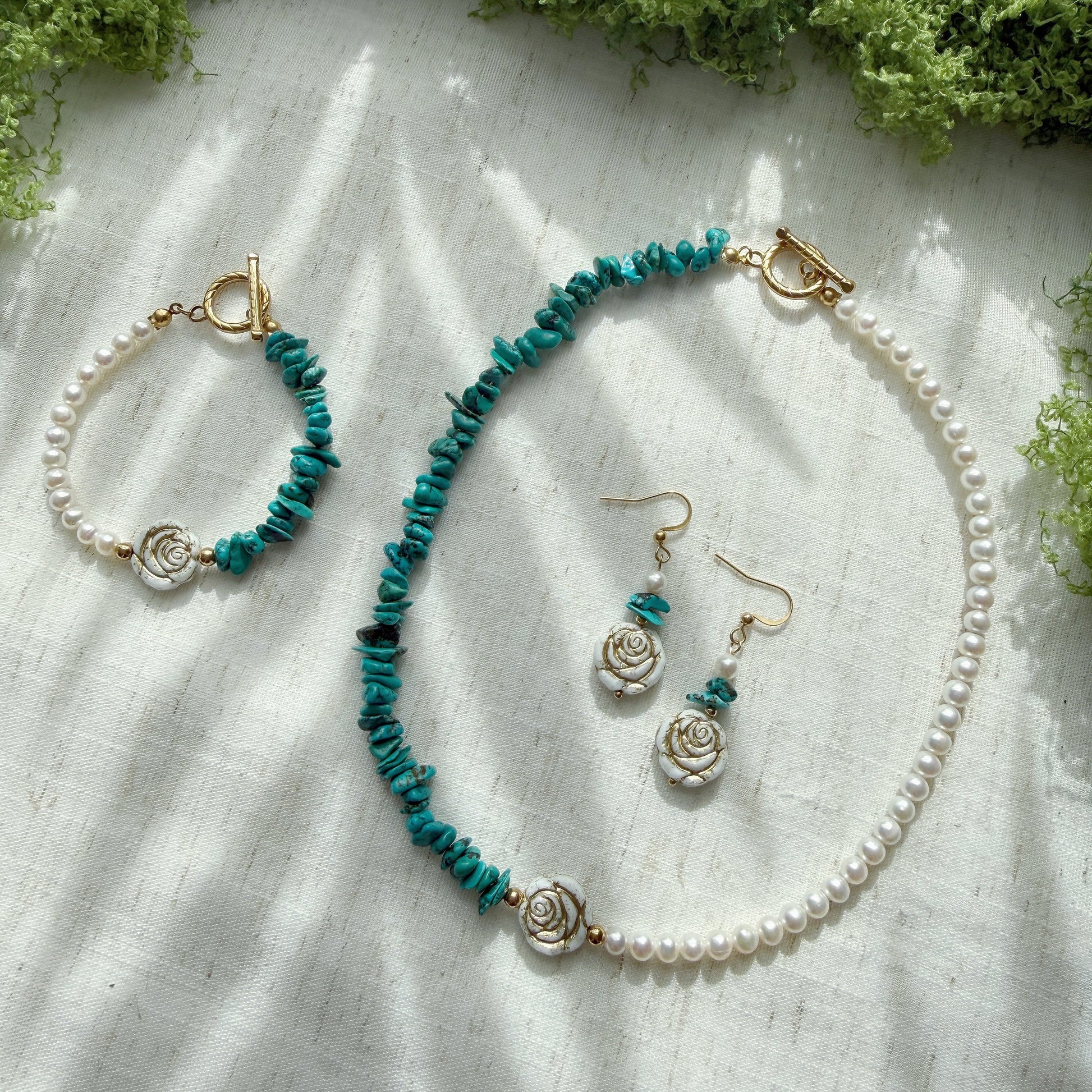Handmade jewelry set featuring natural turquoise, freshwater pearls, and Czech glass rose beads, including a necklace, bracelet, and matching earrings displayed on a soft linen background.
