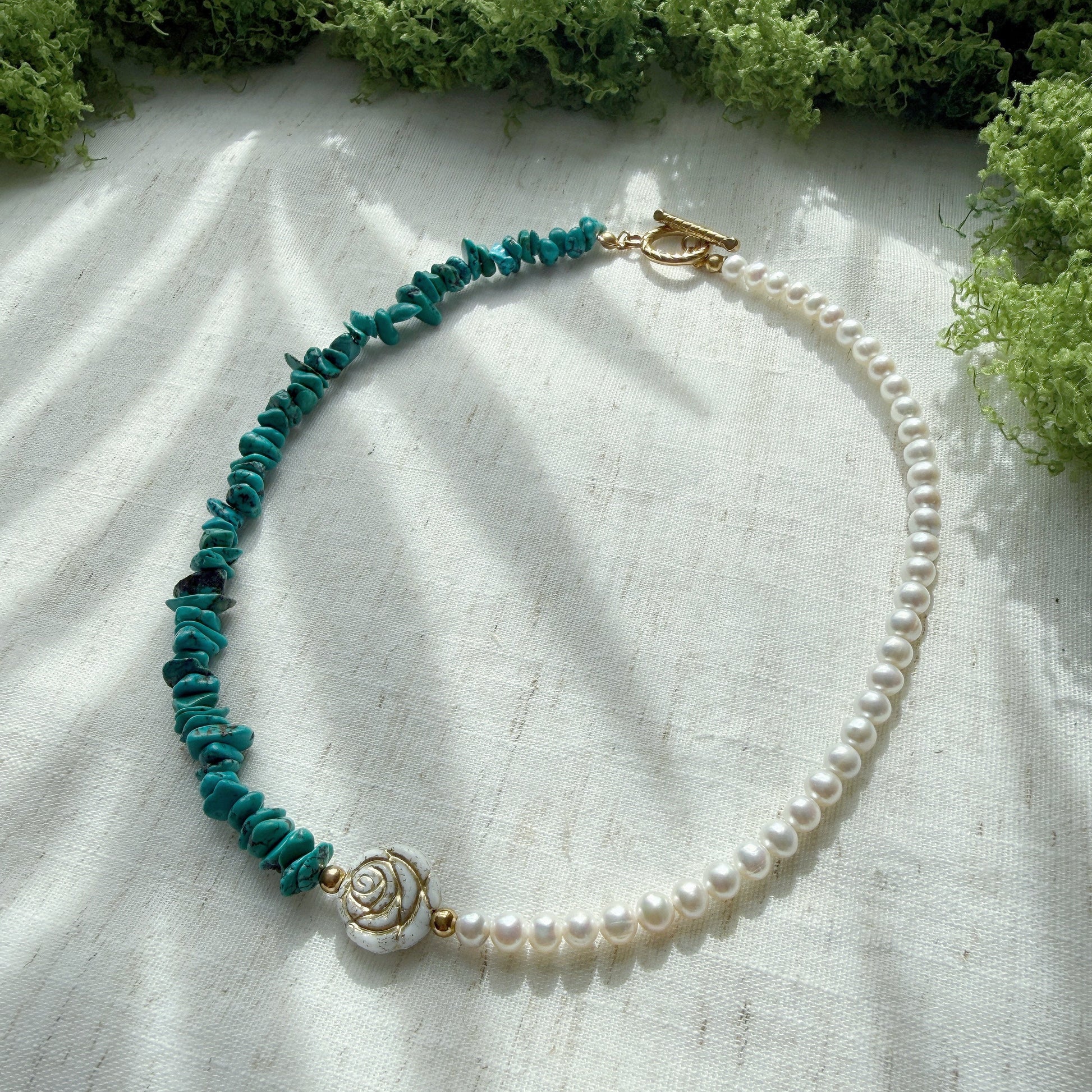 Handmade necklace featuring natural turquoise, freshwater pearls, and Czech glass rose beads on a soft linen background.