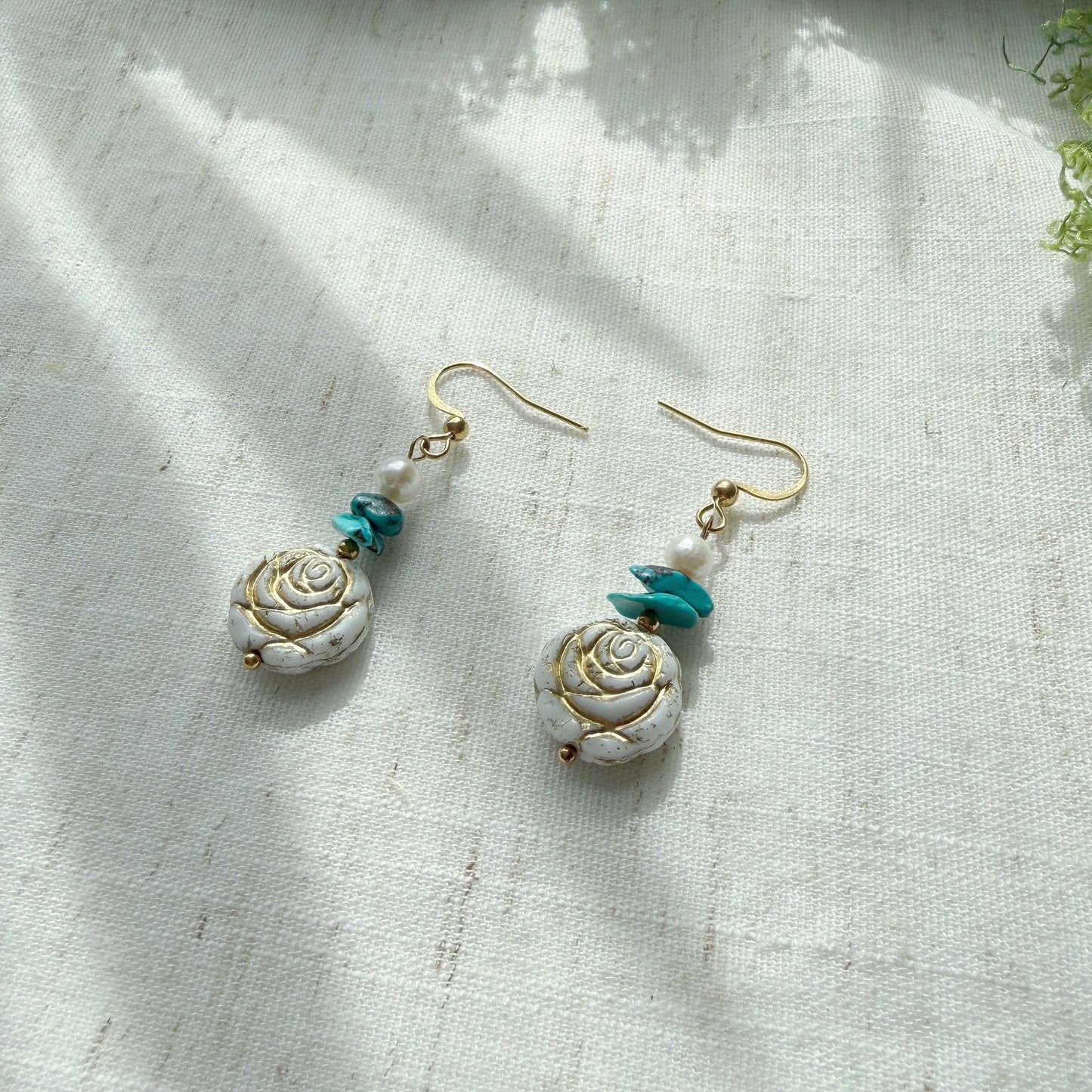 Handmade earrings featuring natural turquoise, freshwater pearls, and Czech glass rose beads displayed on a soft linen background.