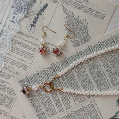 A jewelry set featuring a freshwater pearl necklace and matching drop earrings agate beads and gold-toned hooks, styled on vintage dictionary pages with lace.