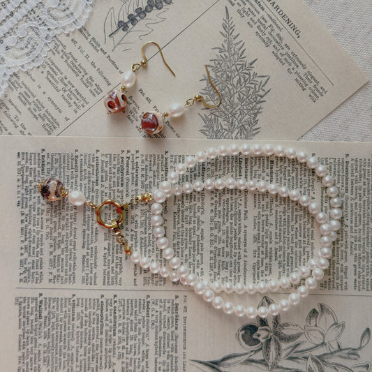 A jewelry set featuring a pearl necklace and matching drop earrings with natural agate and pearl charms, styled on vintage book pages with lace.