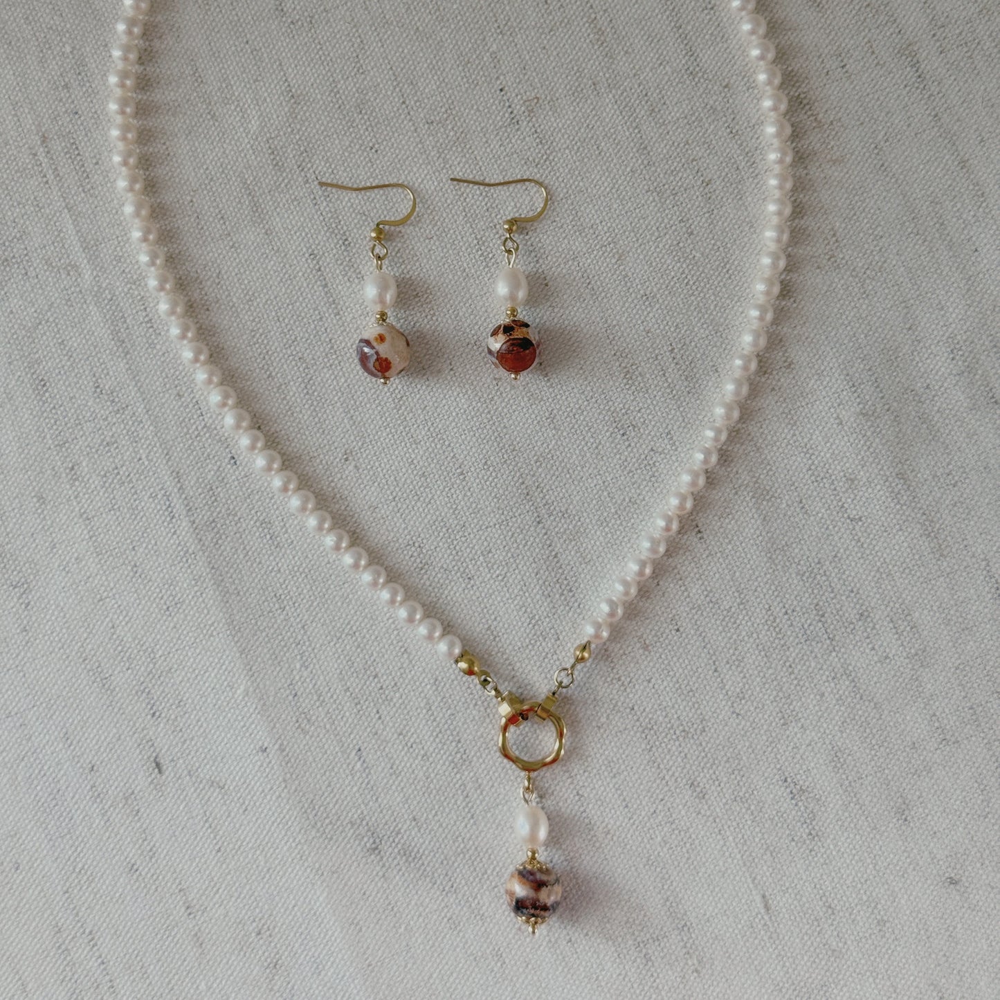A jewelry set featuring a freshwater pearl necklace and matching drop earrings agate beads and gold-toned hooks, styled on vintage dictionary pages with lace.