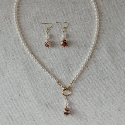 A jewelry set featuring a freshwater pearl necklace and matching drop earrings agate beads and gold-toned hooks, styled on vintage dictionary pages with lace.