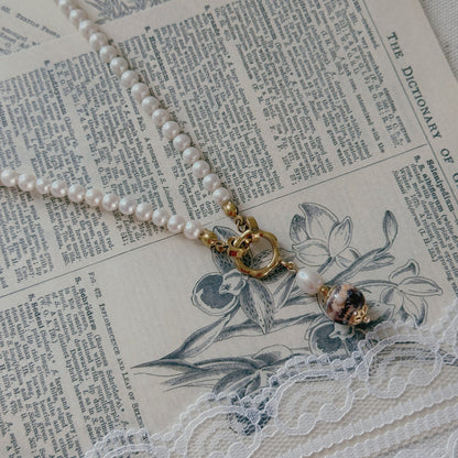A pearl necklace with a gold clasp and a freshwater pearl and agate bead pendant, styled on vintage book pages with white lace.