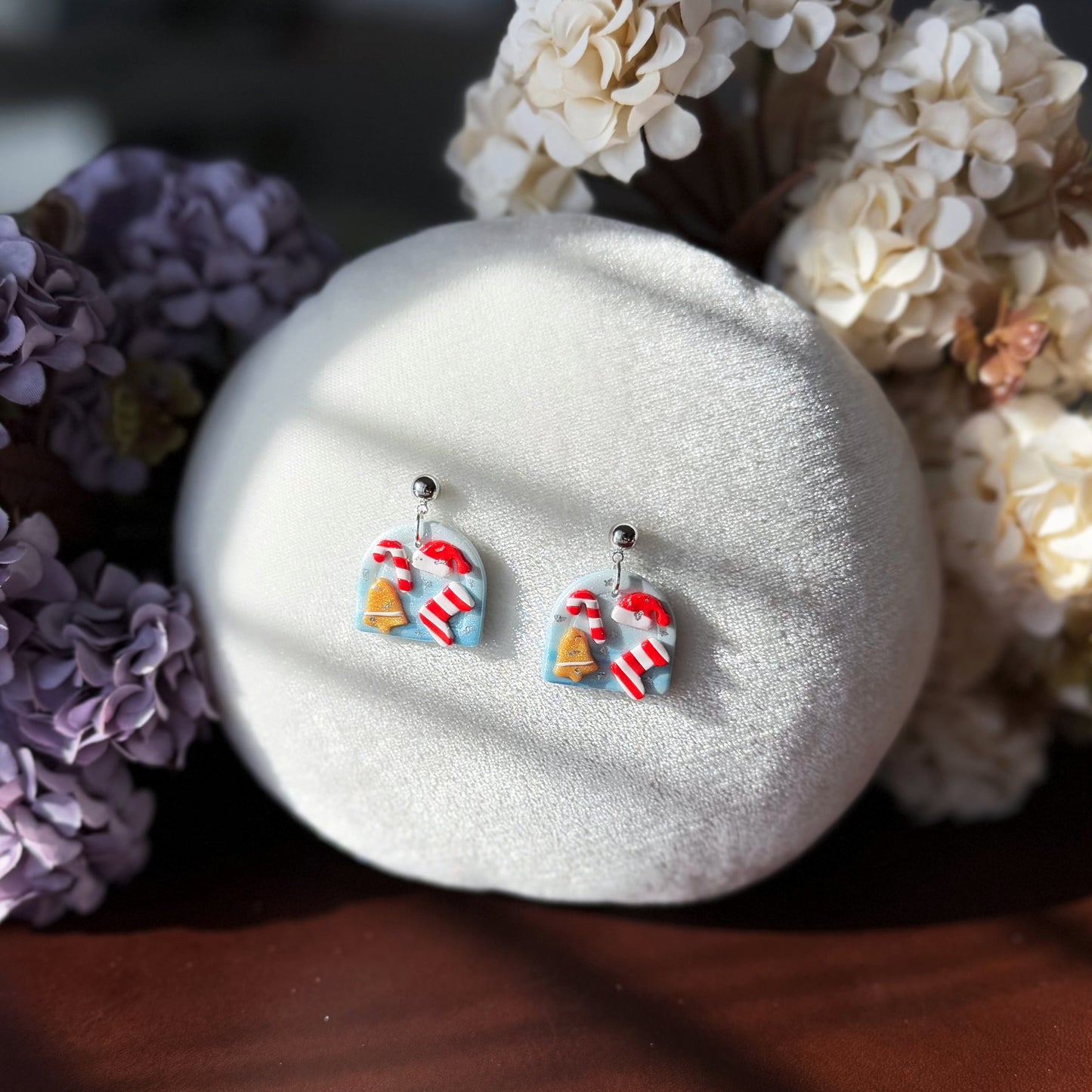 Pair of Christmas effect colorful earrings on a white stone with flowers in the background