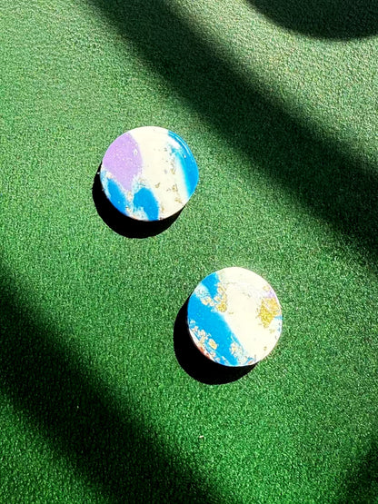 A pair of round earrings with a colorful marble pattern on a green surface
