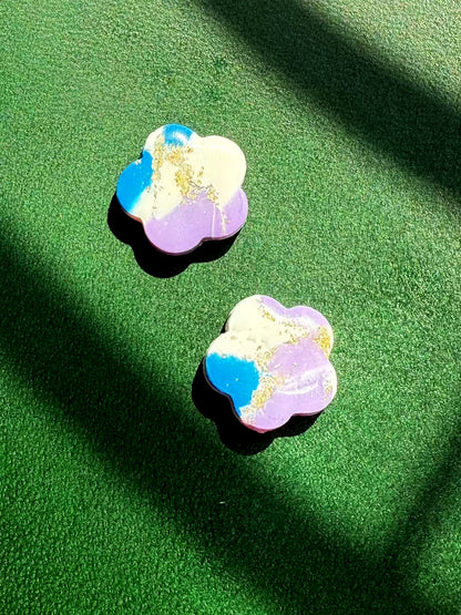 A pair of flower-shaped earrings with a colorful marble effect on a green surface