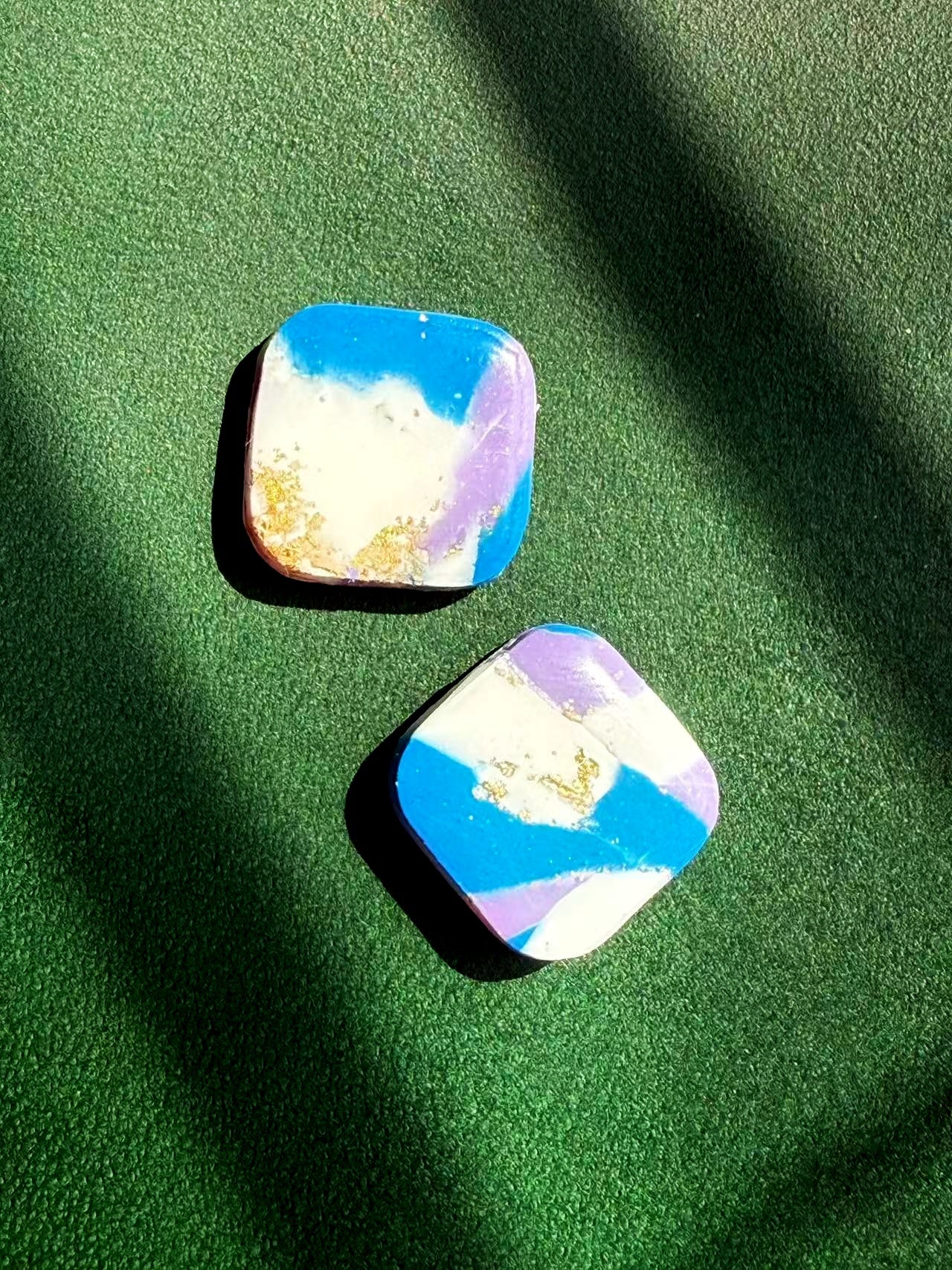 A pair of square-shaped earrings with a colorful marble effect on a green surface