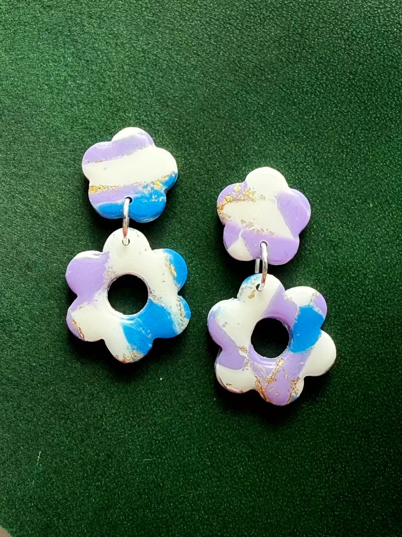 Flower-shaped earrings with purple and blue marble effect on a green background