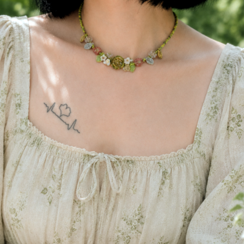 Person wearing a floral dress and a floral beaded necklace sitting outdoors.