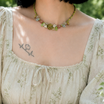 Person wearing a floral dress and a floral beaded necklace sitting outdoors.